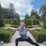 Person in Yoga-Pose im Freien, umgeben von Bäumen und gepflegtem Garten.