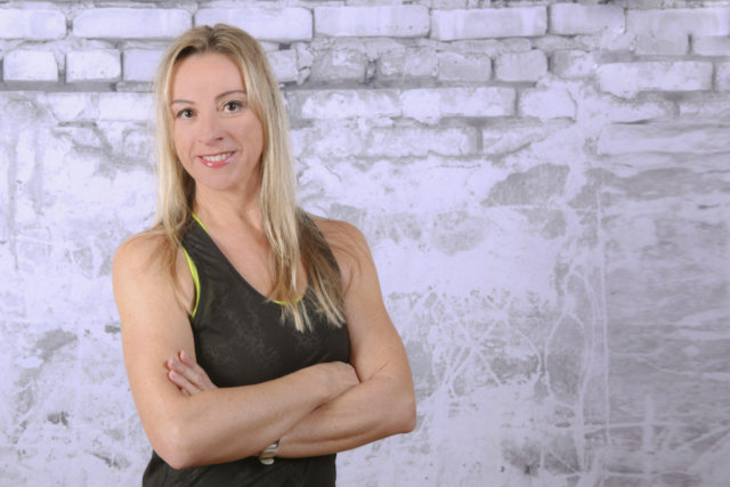 Frau mit blonden Haaren vor einer gemusterten Wand im Fitness-Outfit.