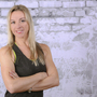 Frau mit blonden Haaren vor einer gemusterten Wand im Fitness-Outfit.