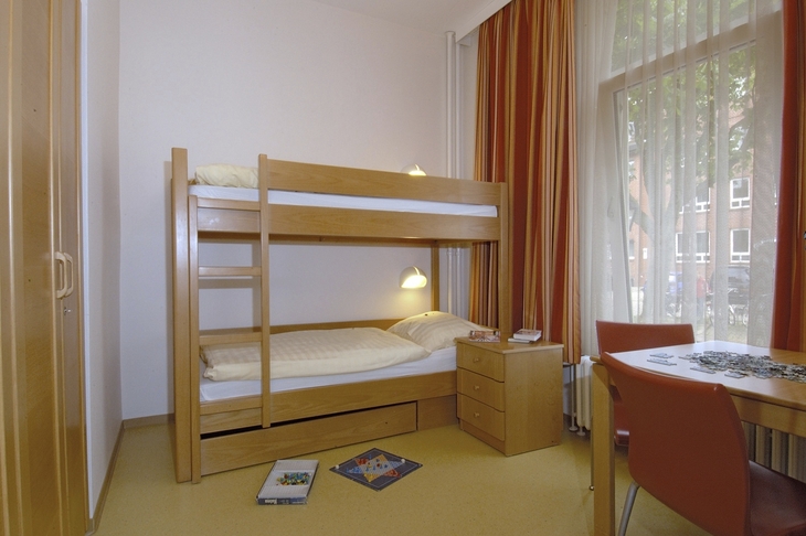 Zimmer mit Etagenbett, Tisch, Stühlen und Fenstervorhängen.