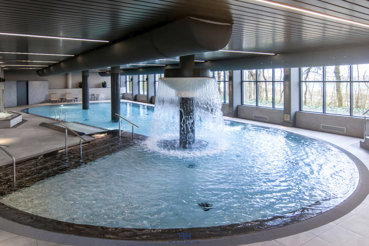 Poolbereich in einem modernen Innenraum mit Wasserfall und großen Fenstern.