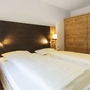 Gemütliches Schlafzimmer in der Ferienanlage Titisee mit Doppelbett mit hohem Kopfteil, Nachttischen und Lampen und einem dreitürigen Holzschrank.