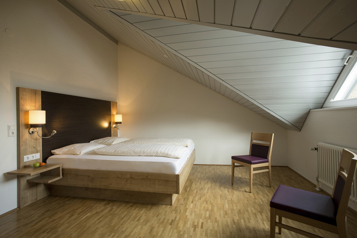 Schlafzimmer in der Ferienanlage Titisee, mit Dachschräge, Holzfußboden, Doppelbett und zwei Stühlen..