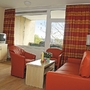 Wohnzimmer mit roten Sesseln und Sofa, Fernseher und großem Fenster.