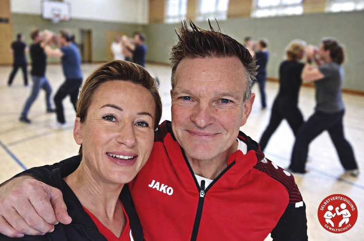Trainerpaar in Turnhalle mit Menschen im Hintergrund beim Training
