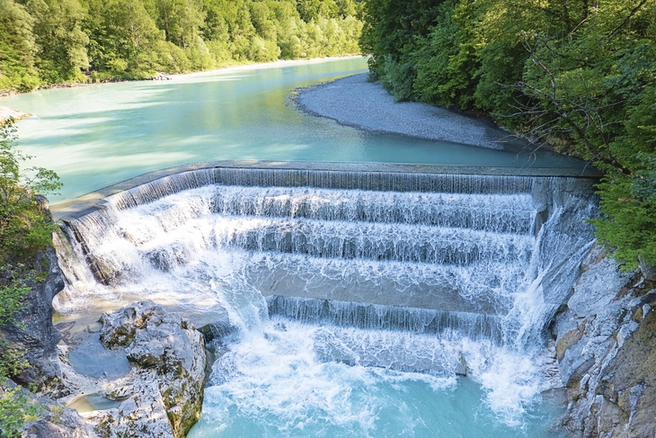 Wasserfall Lechfall in Füssen mit türkisfarbenem Wasser und Wald im Hintergrund.