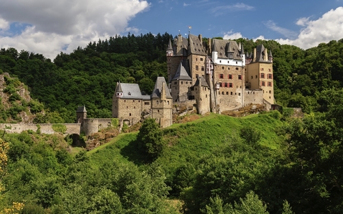 Burg Eltz inmitten grüner Hügellandschaft bei sonnigem Wetter.