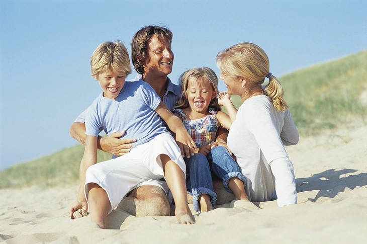 Eine Familie sitzt lächelnd im Sand am Strand.