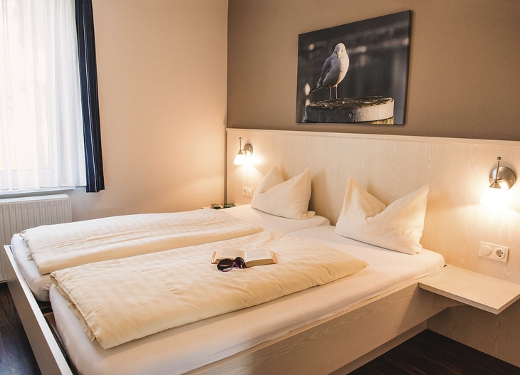 Schlafzimmer in der Ferienanlage Büsum, mit Doppelbett, Wandbild mit einer Möwe sowie einem Fenster mit Vorhängen.