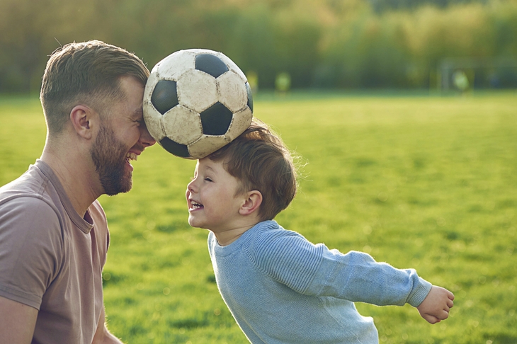 Vater und Kind spielen fröhlich mit einem Fußball auf einer Wiese.