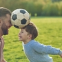 Vater und Kind spielen fröhlich mit einem Fußball auf einer Wiese.