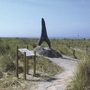 Skulptur eines großen Haifischzahns in einer Dünenlandschaft.