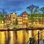 Häuserreihe entlang eines Kanals in Amsterdam bei Nacht, beleuchtet.