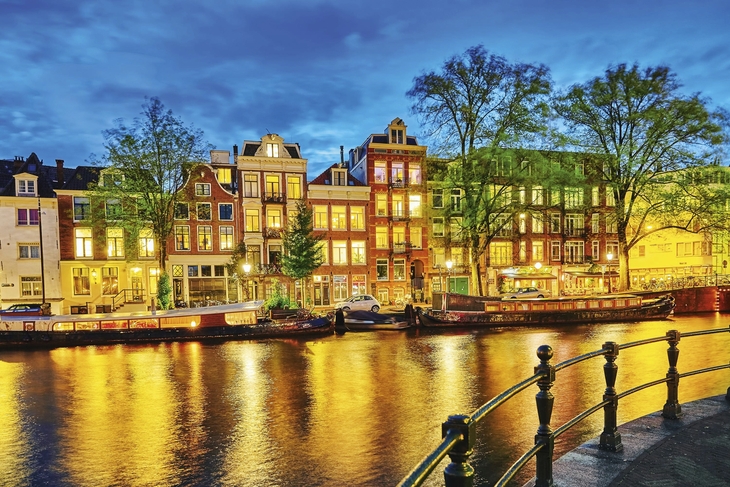 Häuserreihe entlang eines Kanals in Amsterdam bei Nacht, beleuchtet.