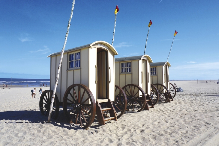 Drei historische Badewagen am Strand von Norderney bei sonnigem Wetter.