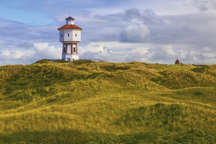 Leuchtturm auf der Insel Langeoog, umgeben von grasbedeckten Dünen unter wolkigem Himmel.