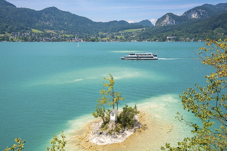 Schiff auf dem Wolfgangsee, umgeben von Bergen und kleiner Insel im Vordergrund.