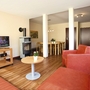 Wohnzimmer in der Ferienanlage Prüm, mit rotem Sofa und Sessel, kleinem runden Tisch, Kaminofen, Fernseher und Esstisch mit Stühlen.