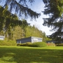 Anthrazitfarbene Bungalows mit Flachdach, der Ferienanlage Prüm, mit weißen Fenstern, auf einer grünen Wiese, umgeben von Bäumen bei Sonnenschein.