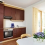 Dunkelrote Küche mit Herd, Backofen und Spüle in der Ferienanlage Prüm, sowie einem Esstisch und Blumenarrangement. Im hinteren Teil sieht man ein großes Fenster mit gelben Vorhängen.