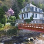 Ein Haus in Monschau mit Brücke über einen Bach und umgeben von Bäumen.