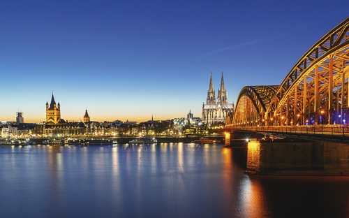 Kölner Dom und beleuchtete Hohenzollernbrücke bei Nacht.