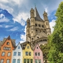 Groß St. Martin Kirche in Köln mit bunten Häusern im Vordergrund bei sonnigem Wetter.