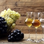 Drei Gläser Grappa mit Trauben im Hintergrund auf Holzuntergrund.