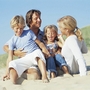 Eine Familie sitzt lächelnd im Sand am Strand.