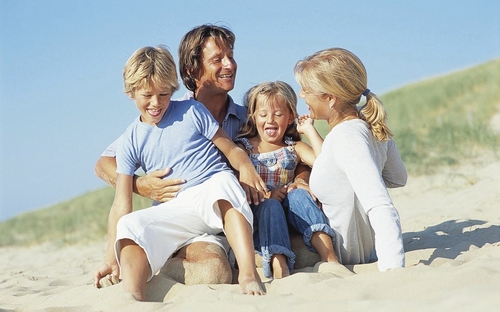 Eine Familie sitzt lächelnd im Sand am Strand.