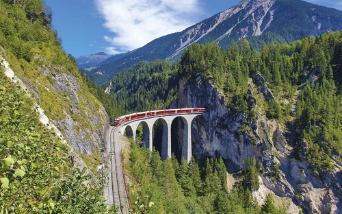 Zug auf der Landwasserviadukt-Brücke in Graubünden, umgeben von Bergen und Wald.