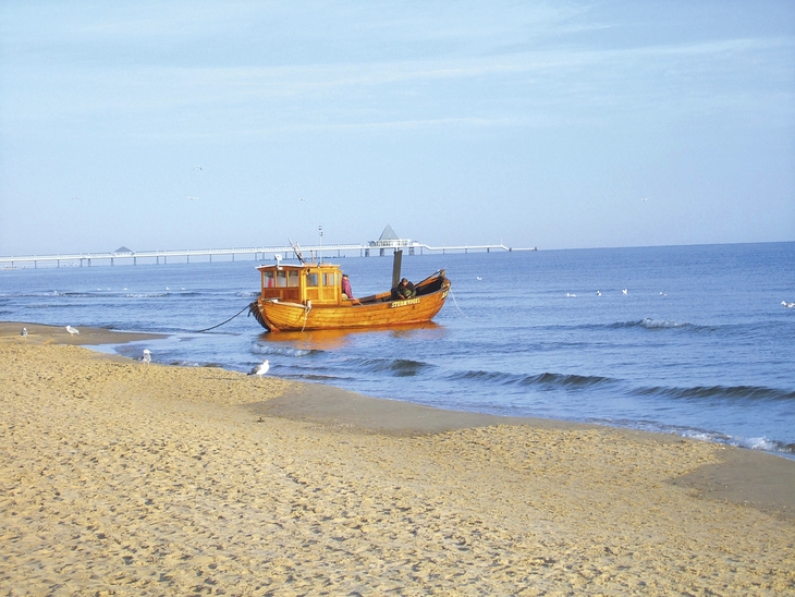 Ein orangefarbenes Boot am Strand mit Seebrücke im Hintergrund.