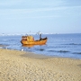 Ein orangefarbenes Boot am Strand mit Seebrücke im Hintergrund.