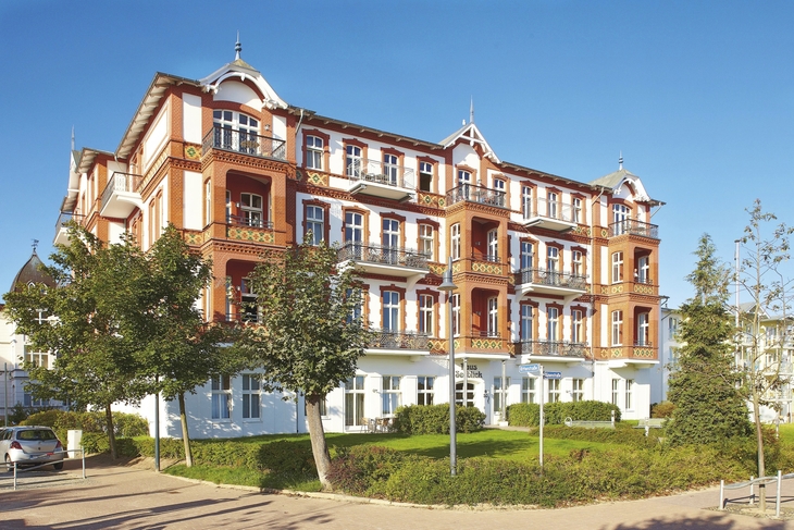 Großes, historisches Gebäude mit roter Fassade in Ferienanlage, blauer Himmel.