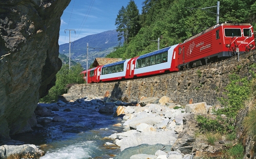 Roter Zug des Glacier Express in malerischer Berglandschaft mit Bach.