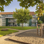 Gebäude mit Rasenfläche, Baum und Spielplatz im Vordergrund.