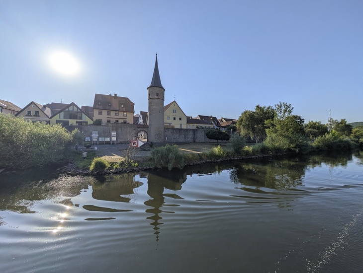 Turm und Gebäude reflektieren im Wasser bei Sonnenlicht in Karlstadt.