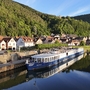 Flusskreuzfahrtschiff an einem sonnigen Tag vor einer bewaldeten Hügellandschaft und Dorf.