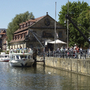 Menschen und Boote entlang einer Promenade am Fluss in Bamberg bei sonnigem Wetter.