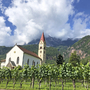 Kirche in Berglandschaft mit Weinreben im Vordergrund.