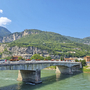 Brücke über einen Fluss mit grüner Landschaft und Bergen im Hintergrund.