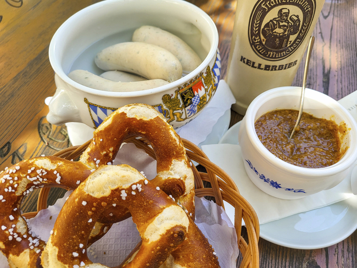 Weißwürste, Brezeln, süßer Senf und Bierkrug auf einem Holztisch.