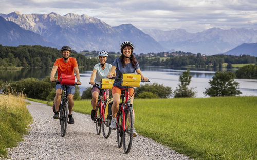 Radfahrer auf Schotterweg mit Blick auf See und Alpen im Hintergrund