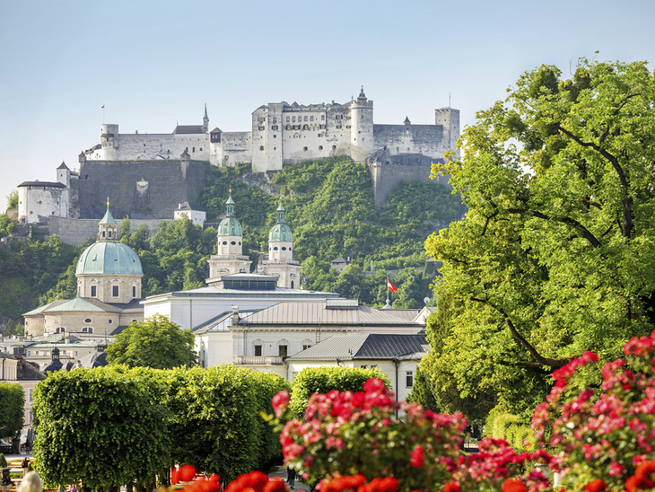 Festung Hohensalzburg über grüner Stadtlandschaft mit blühendem Garten im Vordergrund.