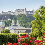 Festung Hohensalzburg über grüner Stadtlandschaft mit blühendem Garten im Vordergrund.