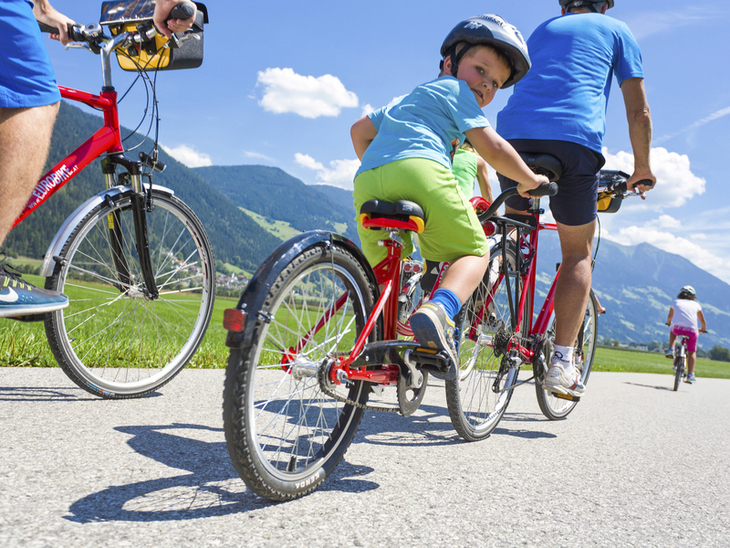 Radfahrer und Kind auf Fahrrädern auf einer ländlichen Straße bei sonnigem Wetter.