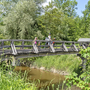 Familie mit Fahrrädern auf hölzerner Brücke über einem Bach in der Natur.