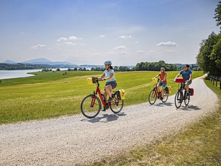 Drei Radfahrer auf einem Schotterweg im Salzburger Seenland bei sonnigem Wetter.