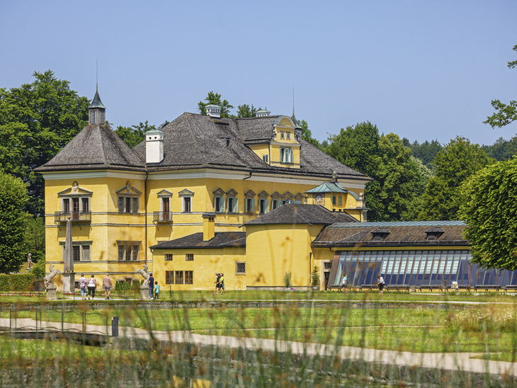 Gelbes historisches Gebäude mit Garten im Vordergrund an einem sonnigen Tag.