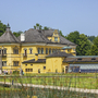 Gelbes historisches Gebäude mit Garten im Vordergrund an einem sonnigen Tag.